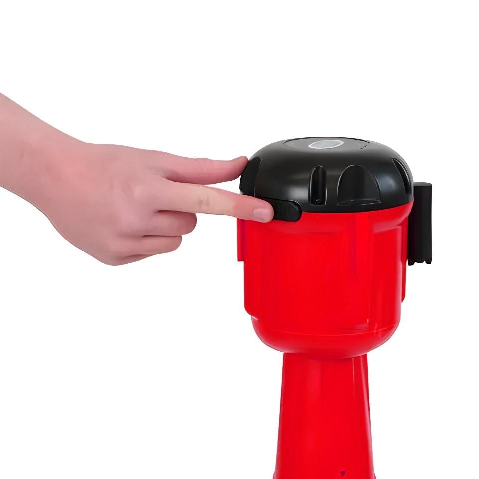 Osoba naciska przycisk na czerwonym sygnalizatorze awaryjnym, który może być używany w sytuacjach kryzysowych. Urządzenie służy do poprawy bezpieczeństwa pracy oraz ochrony środowiska.