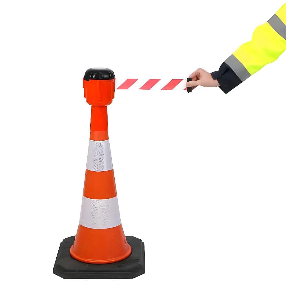 Pracownik w żółtej odzieży ochronnej rozciąga czerwono-białą taśmę ostrzegawczą z ustawionego stożka drogowego, co jest istotnym elementem zarządzania bezpieczeństwem pracy oraz ochroną środowiska w trakcie prac budowlanych lub awaryjnych.