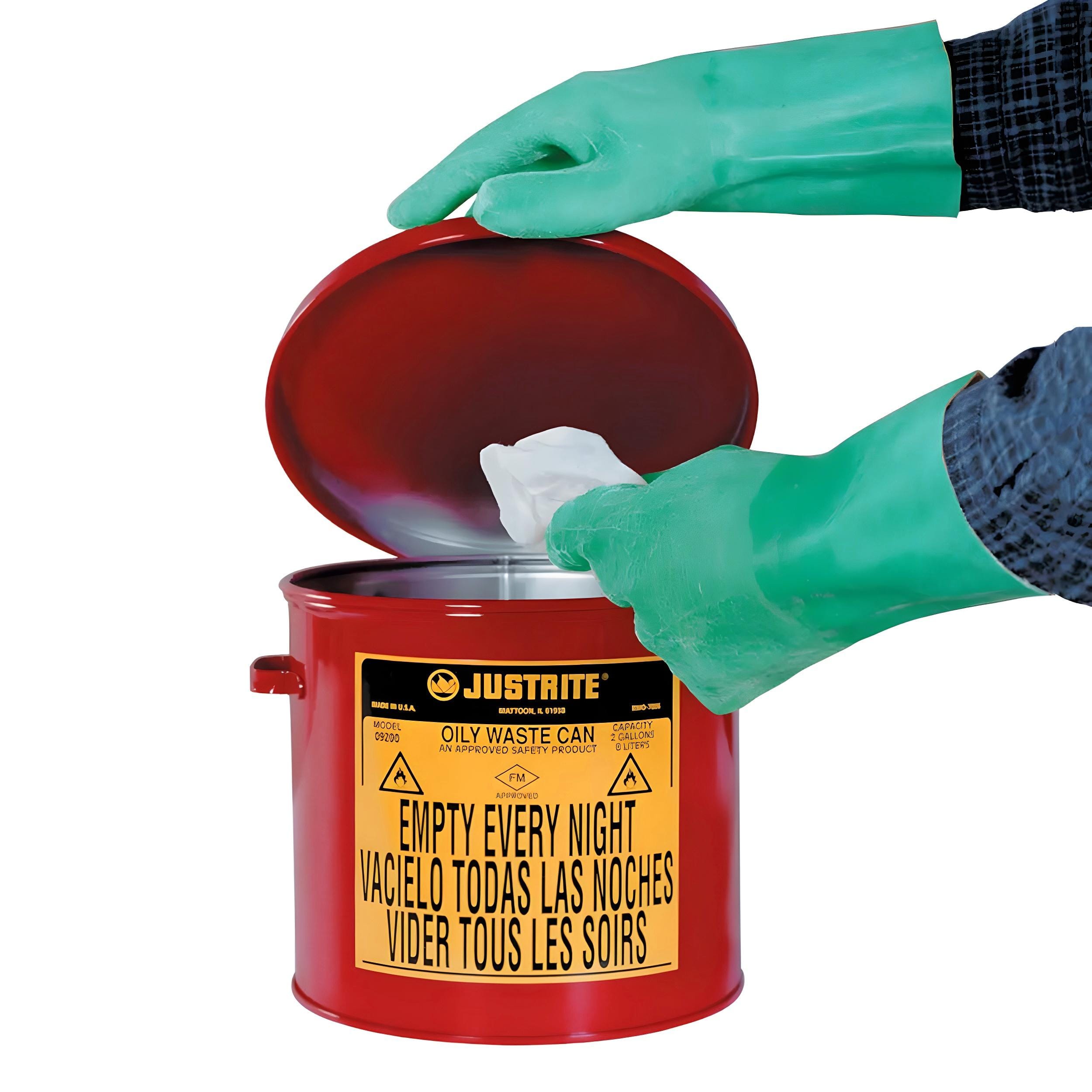 Osoba w zielonych rękawiczkach domowych umieszcza ścierkę w czerwonym pojemniku na odpady olejowe. Pojemnik z etykietą informującą o konieczności codziennego opróżniania, symbolizuje bezpieczeństwo pracy i przyczynia się do ochrony środowiska.
