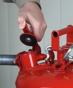 Osoba trzymająca czerwoną gaśnicę i przygotowująca ją do użycia, odblokowując zawór. Obraz ilustruje istotne działania w zakresie bezpieczeństwa pracy oraz środki awaryjne w przypadku pożaru.