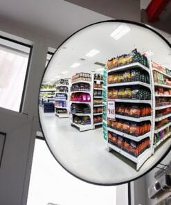Widok wnętrza sklepu z półkami pełnymi produktów spożywczych, ukazany w okrągłym lustrze. Jasne oświetlenie i uporządkowane półki tworzą przemyślaną przestrzeń zakupową. To doskonały przykład dbałości o bezpieczeństwo pracy w handlu detalicznym.