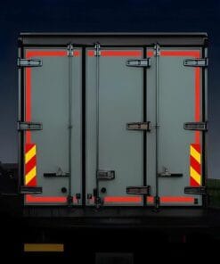 Zblizenie na tylne drzwi przyczepy, kontrastujący szary kolor z czerwonymi i żółtymi elementami odblaskowymi. Podświetlona w ciemności, sugeruje zastosowanie w transporcie towarów. Obraz symbolizuje znaczenie bezpieczeństwa w logistyce i ekologię w transporcie.