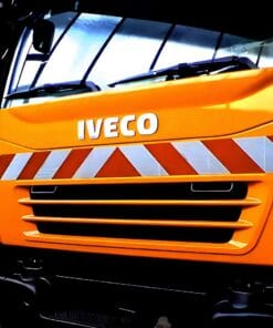 Zbliżenie na pomarańczową ciężarówkę marki Iveco z oznaczeniami bezpieczeństwa, w tym odblaskowymi paskami, podkreślającymi środki awaryjne w transporcie i ochronie środowiska.