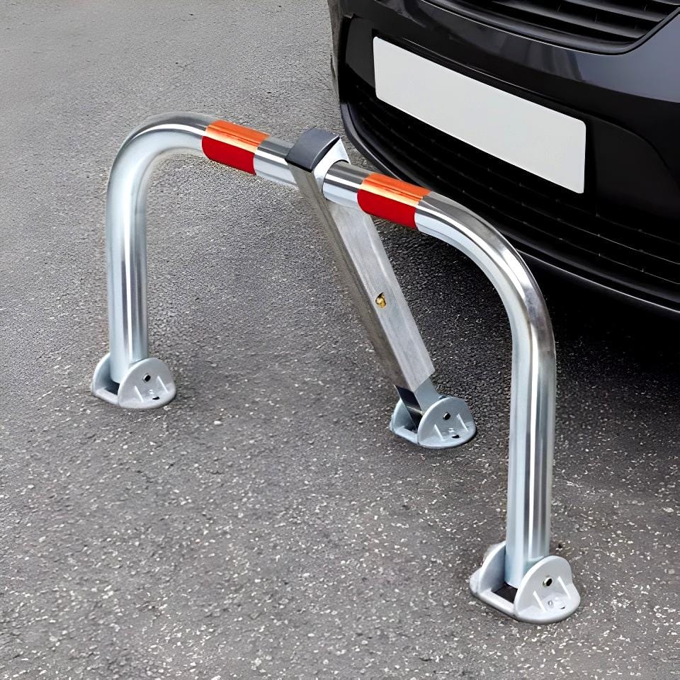 Zamek parkingowy wykonany ze stali nierdzewnej, ustawiony na asfalcie przed samochodem. Elementy zabezpieczające w kolorze czerwonym i białym. Używany do kontroli dostępu i ochrony miejsc parkingowych, co jest istotne dla bezpieczeństwa pracy i ekologii.