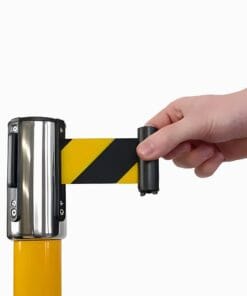 Ręka trzymająca taśmę ostrzegawczą w czarno-żółte paski, wyciąganą z uchwytu montowanego na słupku. Taśma służy do oznaczania obszarów roboczych i zapewnienia bezpieczeństwa w razie zagrożeń. Idealna do zastosowań w ochronie środowiska i bezpieczeństwa pracy.
