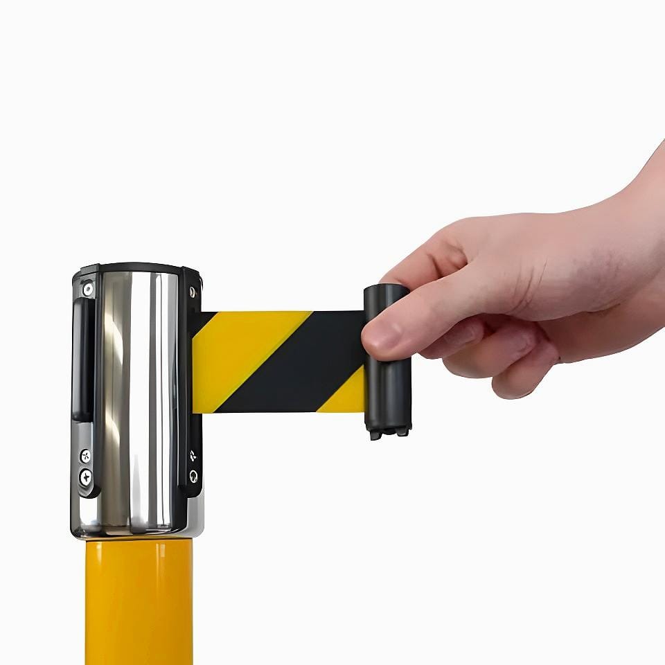 Ręka trzymająca taśmę ostrzegawczą w czarno-żółte paski, wyciąganą z uchwytu montowanego na słupku. Taśma służy do oznaczania obszarów roboczych i zapewnienia bezpieczeństwa w razie zagrożeń. Idealna do zastosowań w ochronie środowiska i bezpieczeństwa pracy.