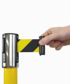 Ręka trzymająca mechanizm do rozwijania pasów ostrzegawczych w kolorze żółto-czarnym, montowany na kolumnie, służący do zabezpieczania przestrzeni i zapewnienia bezpieczeństwa pracy. Ochrona środowiska przed niebezpieczeństwami.