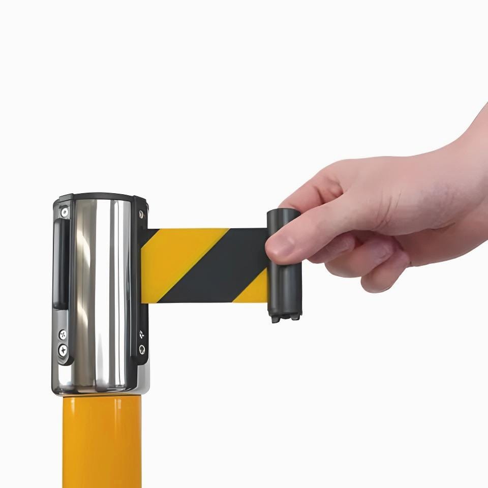 Osoba rozwija taśmę ostrzegawczą w czarno-żółte paski z urządzenia montowanego na słupku, co podkreśla środki awaryjne i bezpieczeństwo pracy w danym obszarze.