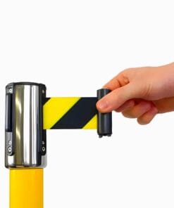 Ręka wyciągająca taśmę ostrzegawczą w czarno-żółte paski z urządzenia montowanego na żółtym słupku. Elementy wskazujące na bezpieczeństwo pracy i użycie środków awaryjnych w celu ochrony środowiska.