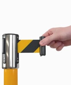 Ręka wyciągająca żółtą i czarną taśmę ostrzegawczą z metalowego uchwytu. Taśma jest używana do oznaczania strefy niebezpiecznej, co podkreśla znaczenie bezpieczeństwa pracy i środków awaryjnych w ochronie środowiska.