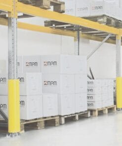 Magazyn z wysokimi regałami, na których znajdują się białe pudełka z logo MPM. W tle widoczne drewniane palety oraz żółte elementy ochronne na krawędziach regałów, co podkreśla bezpieczeństwo pracy w obszarze przechowywania.