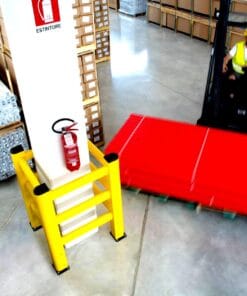 W magazynie widoczny palet z czerwonymi rurkami, obok słupek zabezpieczający z gaśnicą, podkreślony żółtymi barierami ochronnymi, co wskazuje na znaczenie bezpieczeństwa pracy i środków awaryjnych w ochronie środowiska.