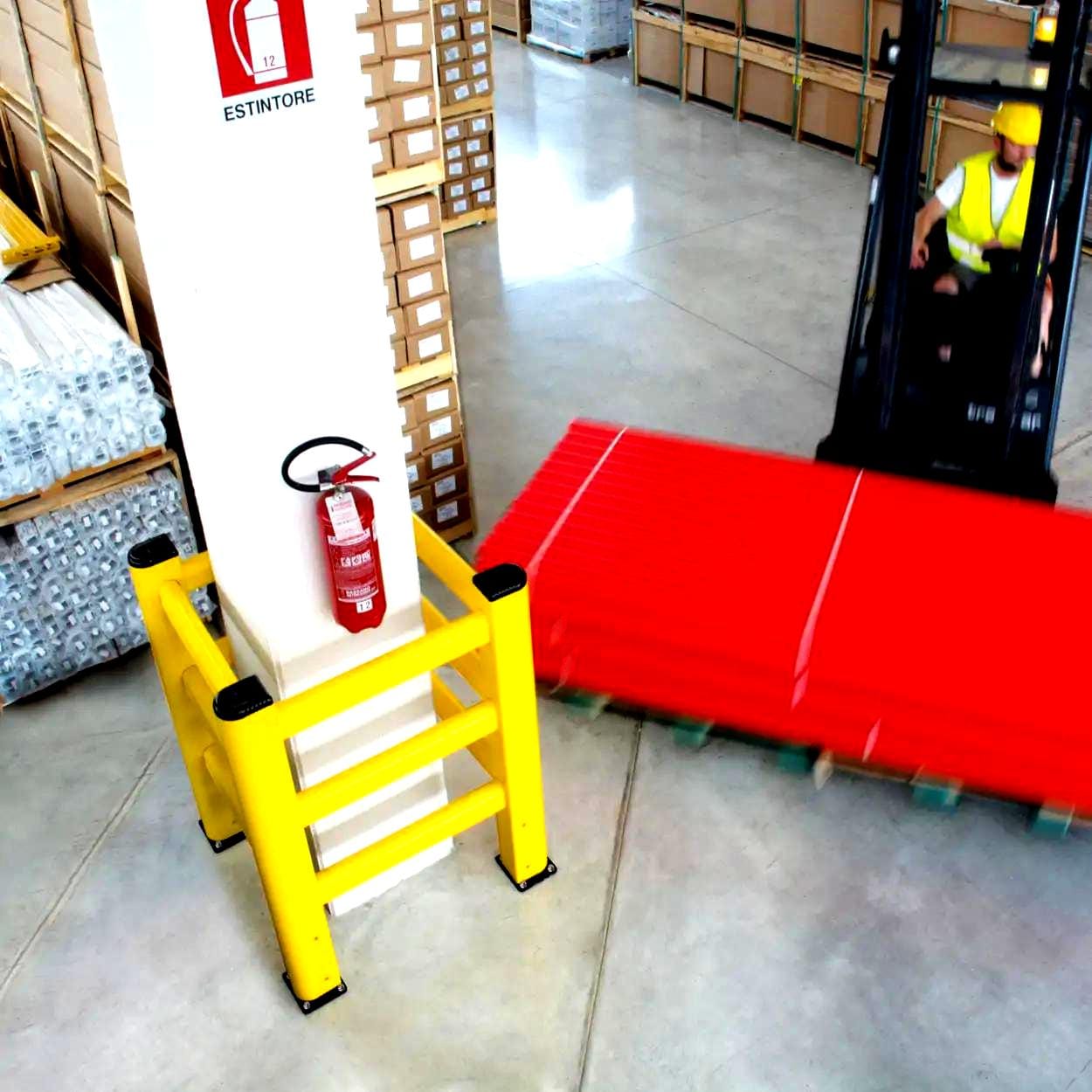 W magazynie widoczny palet z czerwonymi rurkami, obok słupek zabezpieczający z gaśnicą, podkreślony żółtymi barierami ochronnymi, co wskazuje na znaczenie bezpieczeństwa pracy i środków awaryjnych w ochronie środowiska.
