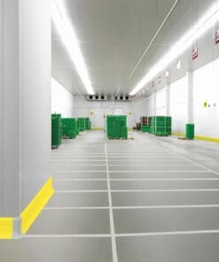 Wnętrze przestronnej chłodni z zielonymi skrzynkami na paletach, dobrze oświetlone sztucznym światłem. Na podłodze widoczne linie wydzielające strefy, co sprzyja bezpieczeństwu pracy i organizacji przestrzeni. Ściany są jasne, a sufit wyposażony w system wentylacji, co jest ważne dla ochrony środowiska.