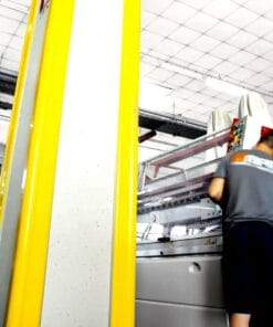 Pracownik obsługujący maszyny w zakładzie produkcyjnym, ze szczególnym uwzględnieniem bezpieczeństwa pracy. Widoczne sprzęty i wyraźne oznaczenia ochrony w tle, podkreślające znaczenie bezpieczeństwa w procesach produkcyjnych i ochrony środowiska.