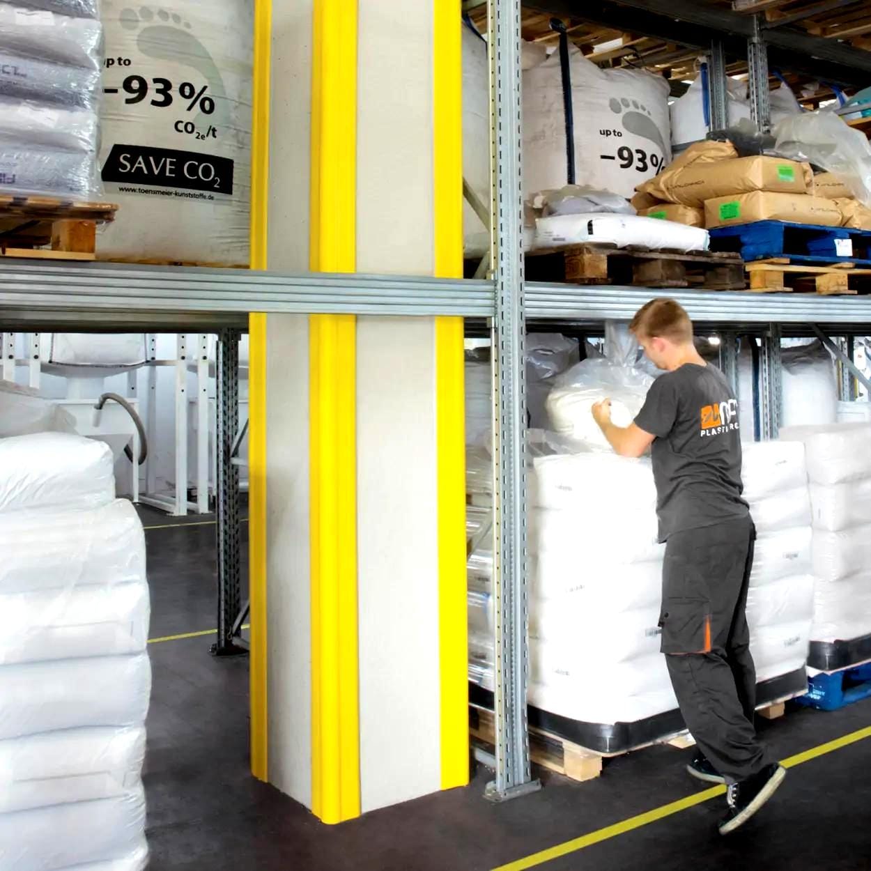 Mężczyzna w magazynie przegląda worki z materiałami ekologicznymi, z wyeksponowanymi oznaczeniami dotyczącymi redukcji emisji CO2, w otoczeniu regałów z towarami. Zdjęcie ilustruje praktyki związane z ochroną środowiska i bezpieczeństwem pracy w przestrzeni magazynowej.