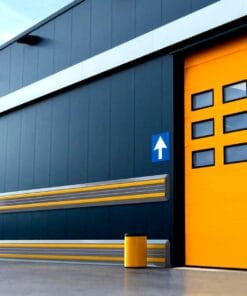 Zewnętrzna ściana nowoczesnego budynku przemysłowego z dużymi żółtymi drzwiami, oznaczeniem kierunkowym oraz elementami bezpieczeństwa, w tym zbiornikiem na odpady. Podkreśla dbałość o środowisko i bezpieczeństwo pracy, z funkcjonalnym i estetycznym designem.