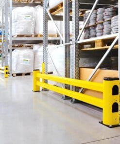 W magazynie widoczne żółte bariery ochronne, które zabezpieczają przestrzeń roboczą. W tle regały z workami i rolkami materiałów. Obraz ilustruje środki awaryjne w kontekście bezpieczeństwa pracy oraz ochrony środowiska.