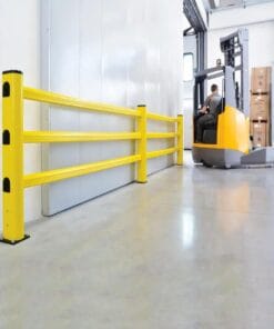 Zdjęcie przedstawia magazyn z żółtymi balustradami ochronnymi oraz wózkiem widłowym w tle, co podkreśla znaczenie bezpieczeństwa pracy i ochrony środowiska w przestrzeniach magazynowych. Wózek widłowy jest używany do transportu towarów w otoczeniu pełnym kartonów.