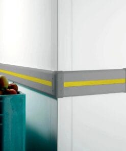 Element ochronny w narożniku pomieszczenia, wykonany z szarego materiału z żółtymi pasami, zapewniający bezpieczeństwo w miejscach przechowywania owoców. Przykład zastosowania zabezpieczeń w środkach awaryjnych w magazynach.