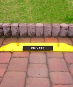 Żółty znak ostrzegawczy "PRIVATE" umieszczony na kostce brukowej, z wyraźnym podziałem na trawniki i ścieżkę, podkreślający ochronę prywatności. Szereg okrągłych kamieni tworzy