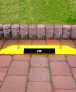 Żółta blokada parkingowa z napisem "VIP" na czerwonym bruku, otoczona trawnikiem i kamiennymi obrzeżami, wskazuje na wydzielone miejsce parkingowe dla osób szczególnie uprzywilejowanych, co podkreśla znaczenie przestrzegania zasad bezpieczeństwa pracy i ochrony środowiska.