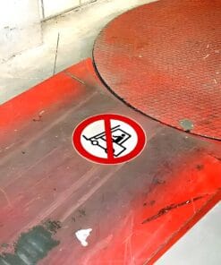 Podłoga z okrągłym obszarem i znakiem zakazu używania wózka, symbolizującym bezpieczeństwo pracy. Zwrócono uwagę na środki awaryjne w przestrzeni roboczej. W tle widać surowe elementy konstrukcyjne oraz ślady użytkowania.
