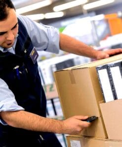 Pracownik skanuje kod kreskowy na paczce w magazynie, co ilustruje proces zarządzania zapasami. Przykład zastosowania odpowiednich środków awaryjnych w pracy, co wpływa na bezpieczeństwo pracy i efektywność operacyjną.