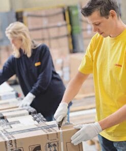 Mężczyzna w żółtej koszulce i białych rękawiczkach otwiera paczkę w magazynie, podczas gdy kobieta w ciemnej koszulce pracuje obok niego. Obraz przedstawia środowisko pracy skoncentrowane na bezpieczeństwie i organizacji, idealne dla ekologicznych środków awaryjnych.