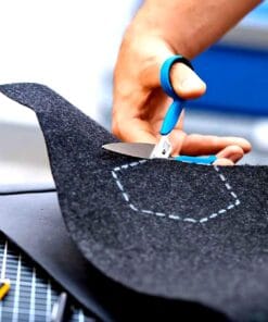 Osoba przycina czarny filc nożyczkami, wykonując precyzyjne cięcie zgodnie z zaznaczoną niebieską linią. W tle widać narzędzia oraz podłoże robocze, co ilustruje proces kreatywnej pracy. Idealne do tematyki ekologii i kreatywnych rozwiązań.