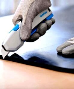 Osoba w rękawicach używa noża do cięcia do precyzyjnego przycinania materiału na płaskiej powierzchni. Narzędzie zapewnia bezpieczeństwo pracy i zwiększa efektywność w procesach obróbczych, co jest istotne w kontekście ochrony środowiska i ekosystemów.