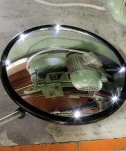 Okrągłe lustro z błyszczącą ramą odbijające silnik oraz mechanizm na podłożu, idealne do oceny stanu maszyn. Używane w środowiskach przemysłowych dla zapewnienia bezpieczeństwa pracy i ochrony środowiska.