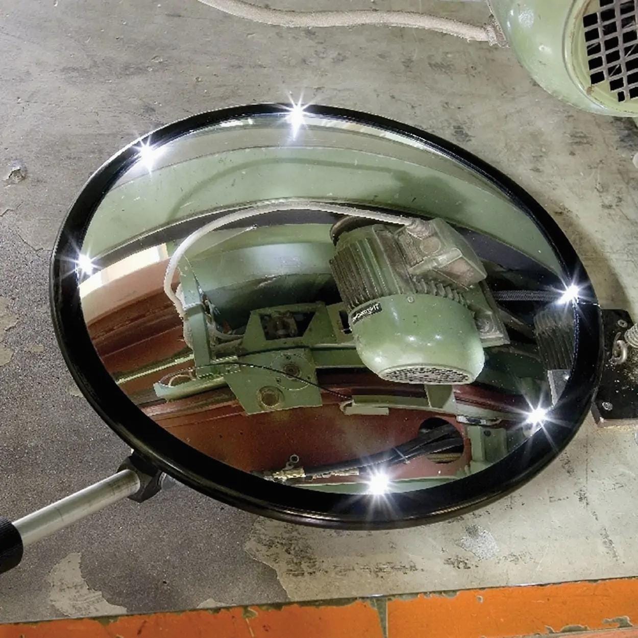Okrągłe lustro z błyszczącą ramą odbijające silnik oraz mechanizm na podłożu, idealne do oceny stanu maszyn. Używane w środowiskach przemysłowych dla zapewnienia bezpieczeństwa pracy i ochrony środowiska.