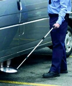 Mężczyzna w mundurze korzysta z długiego narzędzia, aby zbadać przestrzeń pod pojazdem. Obraz ilustruje działania związane z bezpieczeństwem pracy oraz monitorowaniem potencjalnych zagrożeń w obszarze parkingu, co jest istotne w kontekście ochrony środowiska i skutecznych środków awaryjnych.