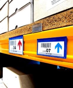 Zdjęcie regału magazynowego z zaznaczonymi poziomami 04 i 07, gdzie widać niebieskie etykiety z kodami kreskowymi i strzałkami wskazującymi kierunek. Pomaga to w identyfikacji i organizacji produktów, co jest istotne dla efektywnego zarządzania zapasami i bezpieczeństwa pracy.