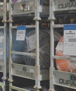 Zdjęcie przedstawia regały magazynowe z workami materiałów, oznaczonymi etykietami. Widać różnokolorowe rolki w folii, co może wskazywać na zastosowanie w przemyśle. Elementy te są kluczowe dla zachowania standardów bezpieczeństwa pracy oraz ochrony środowiska.