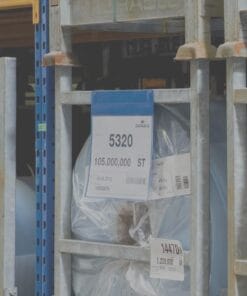 Zdjęcie magazynu z przechowywanymi materiałami. Na metalowych półkach widoczne są oznaczenia i etykiety, w tym numer partii 5320 oraz ilość 105.000.000 ST. Elementy te mogą być związane z bezpieczeństwem pracy i efektywnością zarządzania zasobami.