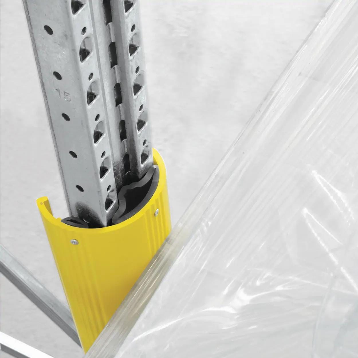 Zbliżenie na metalowy stojak regałowy z żółtą osłoną w miejscu połączenia, w tle przezroczysta folia. Elementy te mogą być zastosowane w kontekście bezpieczeństwa pracy oraz ochrony środowiska w magazynach i miejscach przechowywania.