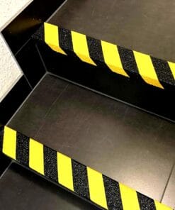 Zdjęcie przedstawia schody z wyraźnymi, żółto-czarnymi pasami ostrzegawczymi na krawędziach stopni. Elementy te zwiększają bezpieczeństwo, zwracając uwagę na niebezpieczeństwo potknięcia. Doskonały przykład środków awaryjnych w przestrzeni publicznej, poprawiający bezpieczeństwo pracy.