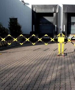 Zabezpieczona strefa przed rampą załadunkową, z żółtym ogrodzeniem ochronnym w kształcie rombów, na kostkowanej nawierzchni. Elementy te zwiększają bezpieczeństwo pracy, zapobiegając dostępowi do niebezpiecznych obszarów.