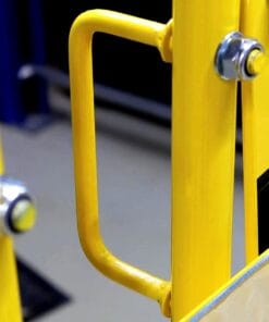 Zbliżenie na żółty uchwyt bezpieczeństwa, umieszczony przy metalowej barierze, z lustrem u dołu. Elementy metalowe podkreślają dbałość o środki awaryjne i bezpieczeństwo pracy w miejscu publicznym.