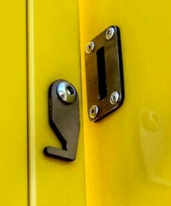 Zbliżenie na zamek w drzwiach pomalowanych na żółto, z metalowym hakiem, śrubami i osłoną. Elementy zapewniają bezpieczeństwo i ochronę, co jest ważne w kontekście bezpieczeństwa pracy i stosowania odpowiednich środków awaryjnych.
