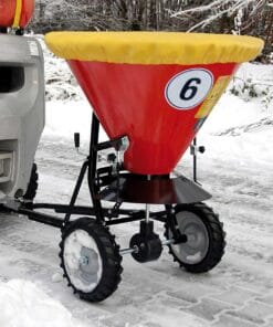 Czerwony rozsiewacz z żółtą krawędzią, przymocowany do maszyny, na zaśnieżonej drodze. Używany do rozsypywania materiałów, co jest ważne w kontekście bezpieczeństwa pracy i ochrony środowiska w warunkach zimowych.
