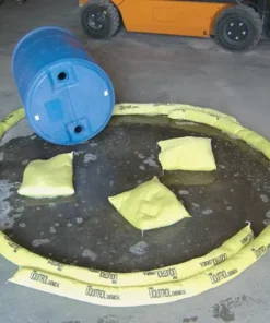 Ujęcie przedstawiające niebieski pojemnik na chemikalia, otoczony żółtymi sorbentami, które zabezpieczają wyciek płynów w magazynie. Wokół pojemnika leżą poduszki sorpcyjne, a w centrum widoczne są plamy cieczy, co podkreśla znaczenie środków awaryjnych w kontekście bezpieczeństwa pracy i ochrony środowiska.