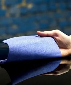 Ręka trzyma niebieską ściereczkę z materiału, odbijającą się na połyskującej powierzchni. Obraz podkreśla jej teksturę, co może być przydatne w kontekście ochrony środowiska i ekologicznym zachowaniu, np. w ramach skutecznych środków awaryjnych.