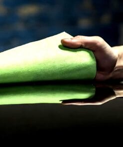 Ręka trzyma zielony ręcznik papierowy, zbliżający się do schyndżowanej powierzchni. Obraz odzwierciedla dbałość o czystość i bezpieczeństwo pracy, podkreślając rolę środków awaryjnych w ochronie środowiska.