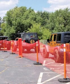Widok parkingu z zaporą w postaci pomarańczowej siatki ochronnej, wzdłuż której parkują cztery terenowe samochody. W tle widać drzewa, co świadczy o ekologicznej okolicy. Zastosowanie zabezpieczeń podkreśla znaczenie środków awaryjnych i bezpieczeństwa pracy.