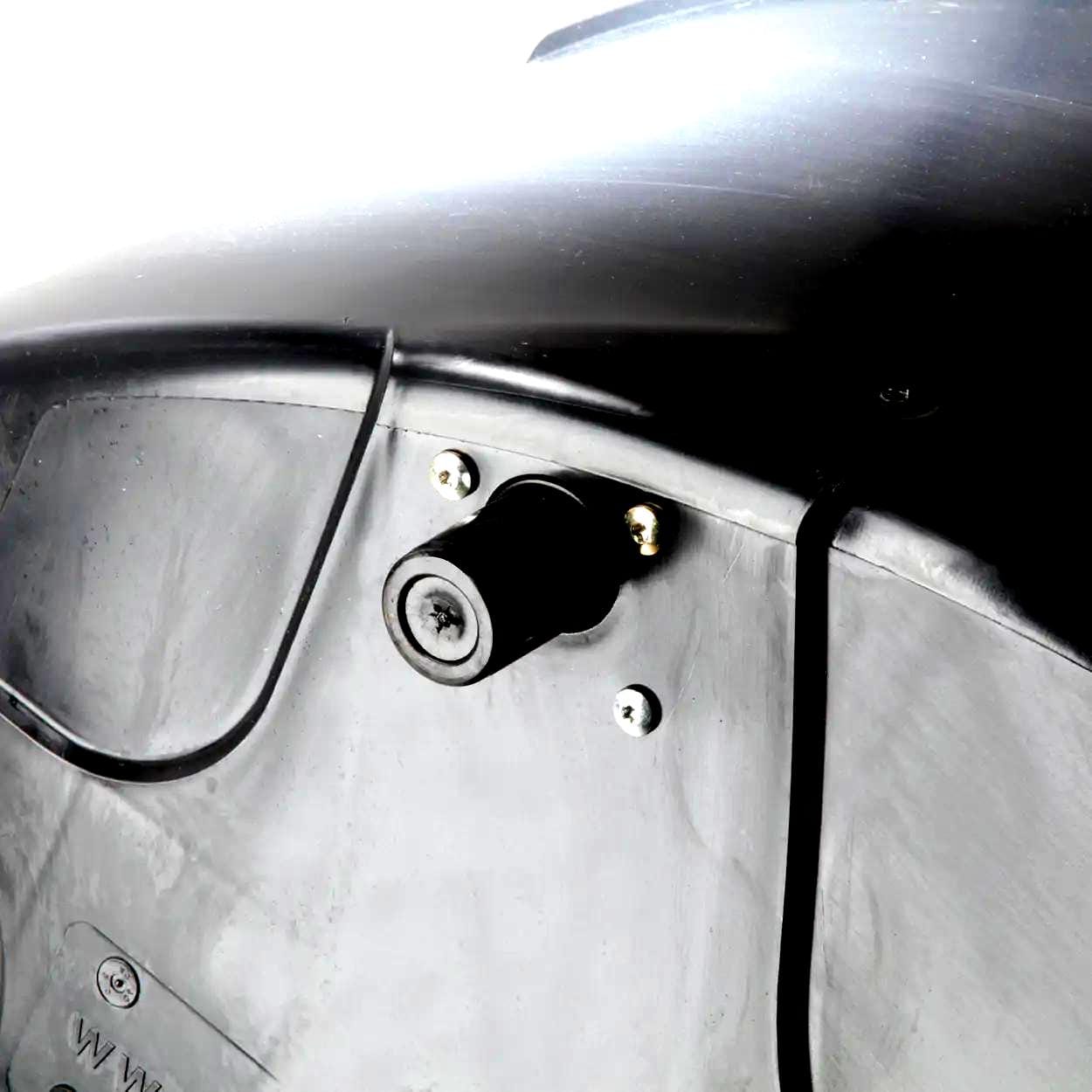 Zbliżenie na złącze elektryczne umieszczone na tle ciemnej obudowy. Element jest zabezpieczony śrubami, co wskazuje na zastosowanie w środowiskach wymagających trwałości i ochrony, podkreślając znaczenie bezpiecznych metod pracy w kontekście ochrony środowiska.