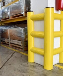 Żółty zabezpieczający słup, umieszczony na rogu magazynu, chroniący ścianę przed uszkodzeniami. W tle widać palety z towarami owiniętymi folią. Elementy te poprawiają bezpieczeństwo pracy i pomagają w ochronie środowiska przemysłowego.
