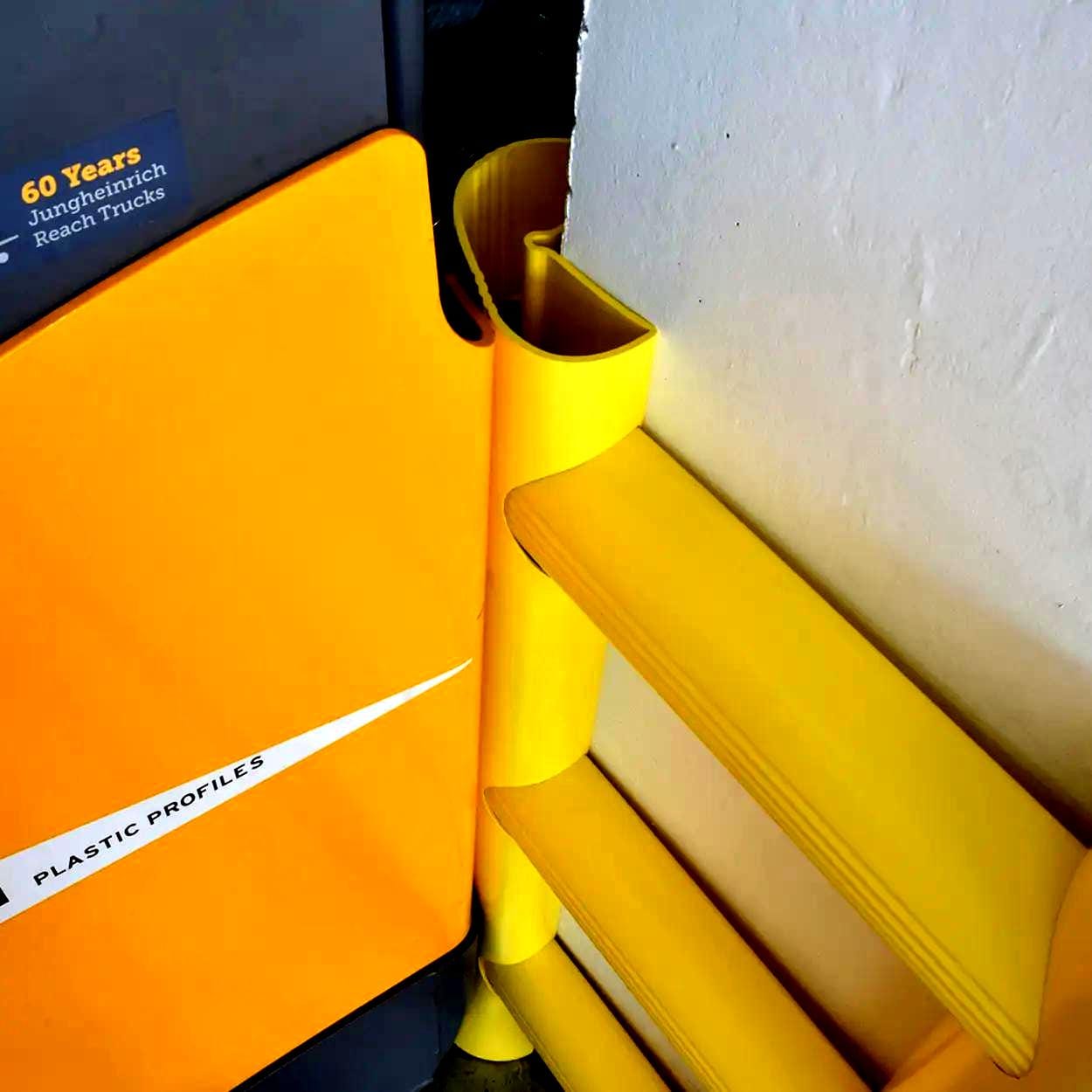 Zdjęcie przedstawia kolorowe, żółte profile plastikowe umieszczone obok wózka widłowego. Elementy te służą do ochrony i zabezpieczenia w miejscu pracy, zapewniając bezpieczeństwo i wspierając zasady ochrony środowiska w przemyśle.